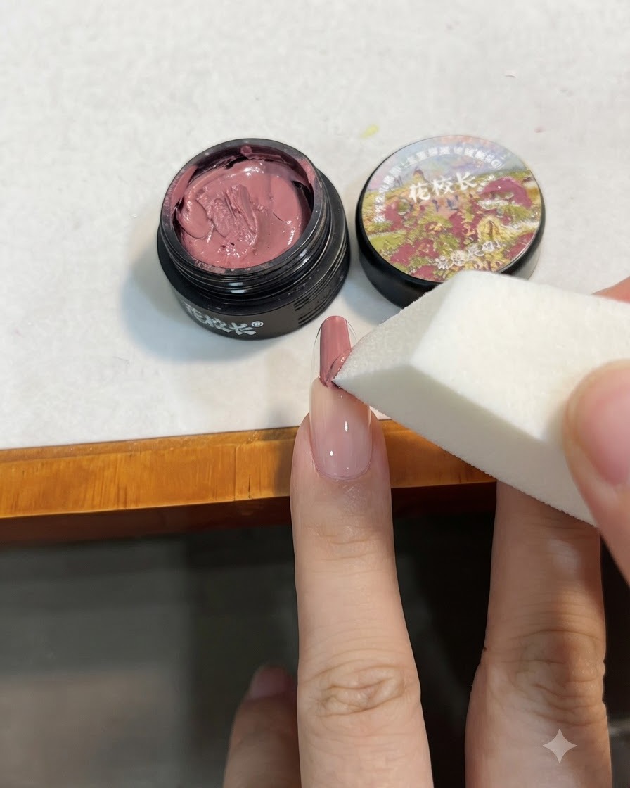 Ein weißer Make-up-Schwamm tupft das rosa Gel auf den Nagel, um es nach unten hin zu verblenden.