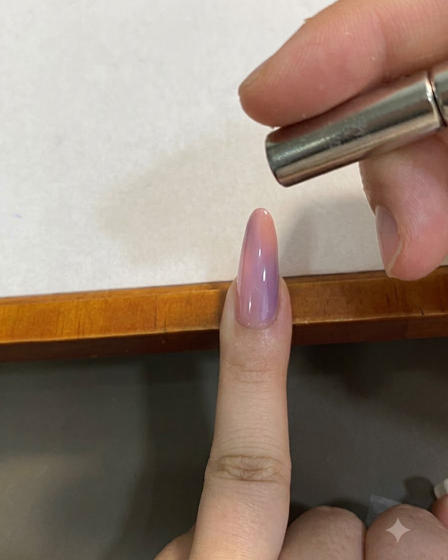 Ein kleiner Magnet wird knapp über einem rosa Farbverlauf-Cat-Eye-Nagel gehalten, um das magnetische Pigment zu formen.