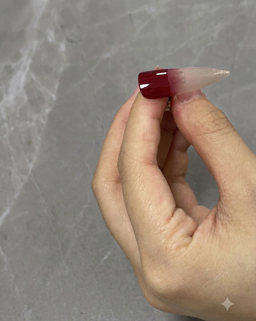 Eine Nahaufnahme eines Nagelpinsels verblendet einen weinroten Farbverlauf nach unten auf einem neutralen Nageltip.
