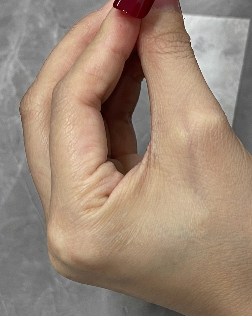 Ein Korrekturpinsel wischt überschüssiges rotes Gel an den Rändern einer Nagelspitze weg.