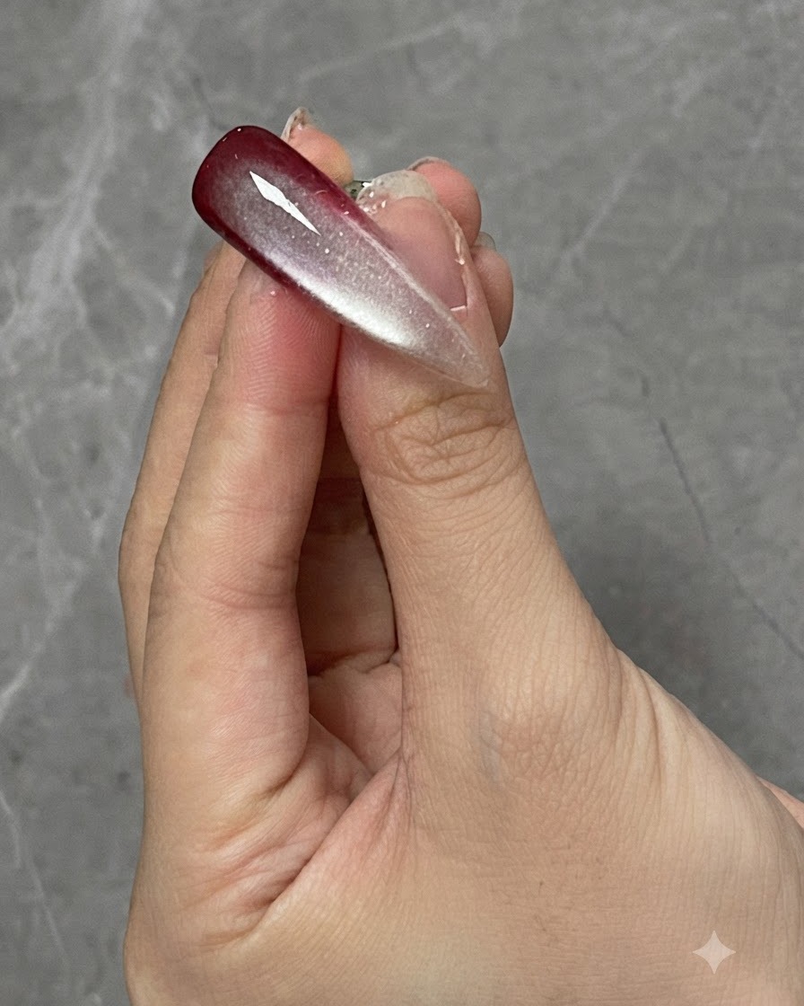 Ein Finger mit einem ausgehärteten Ombré- und Cat-Eye-Nageldesign unter einer Lampe positioniert.