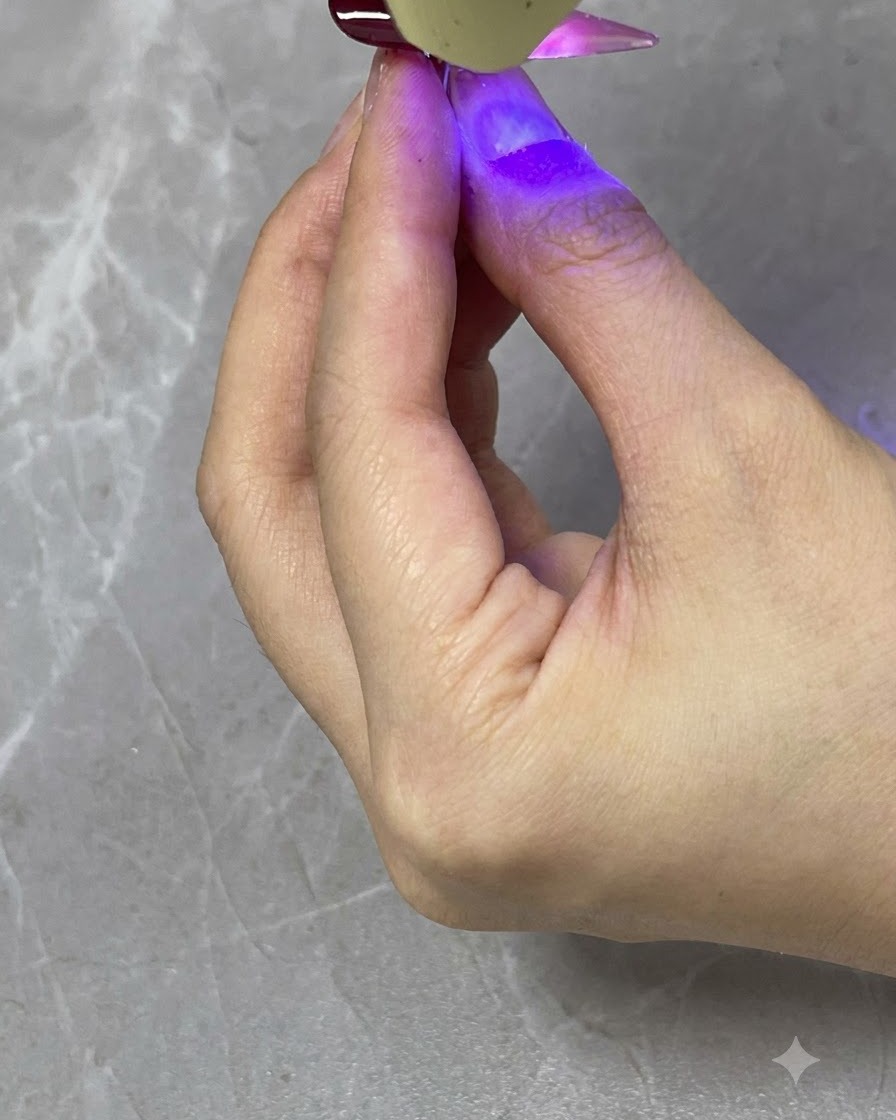 Eine tragbare UV- oder LED-Lampe härtet eine transluzente rote Verlaufsschicht auf einem fertigen Nagel aus.
