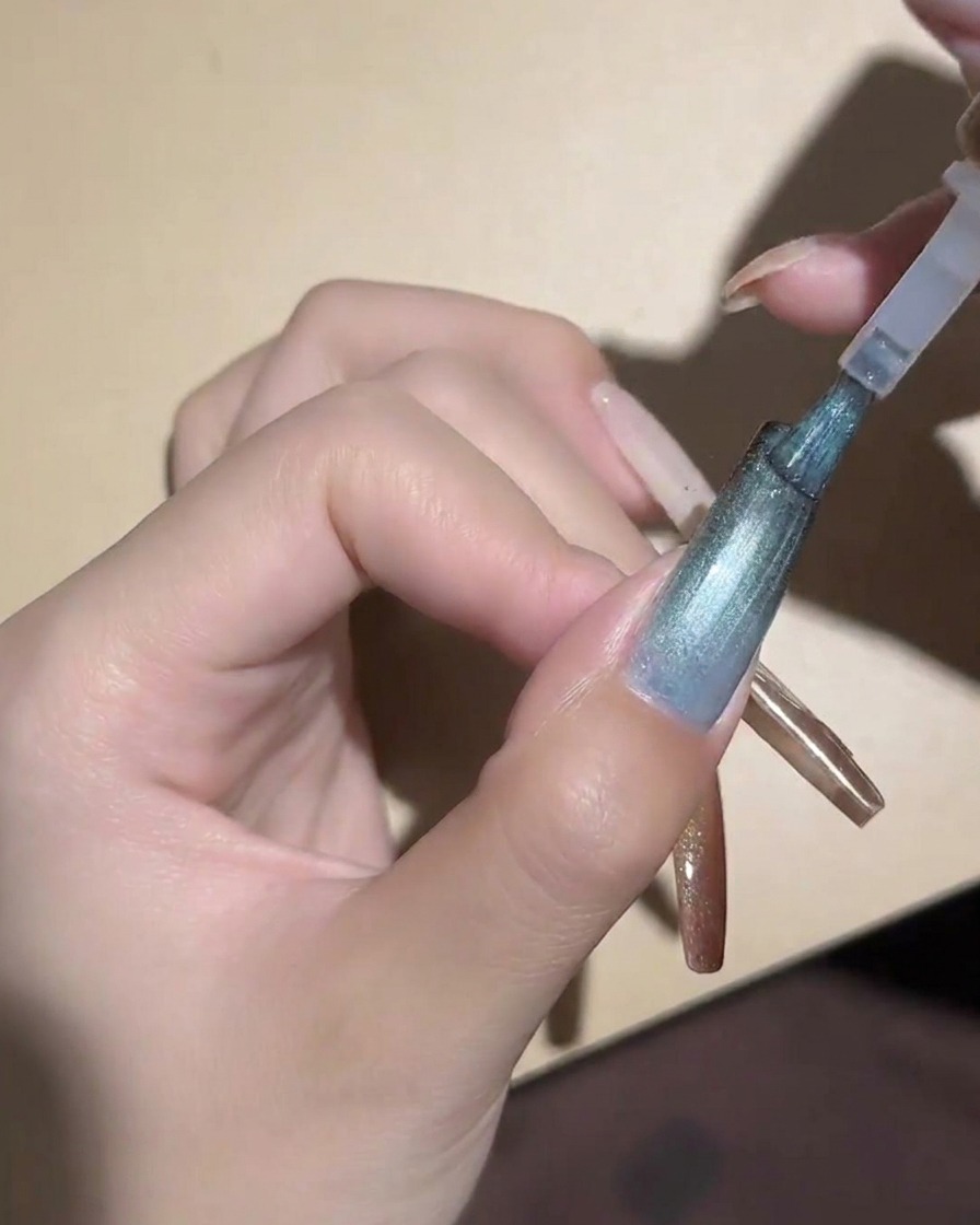 Ein zylindrischer Magnet wird nahe an einen blauen Cat-Eye-Nagel gehalten, um die Partikel zu magnetisieren.