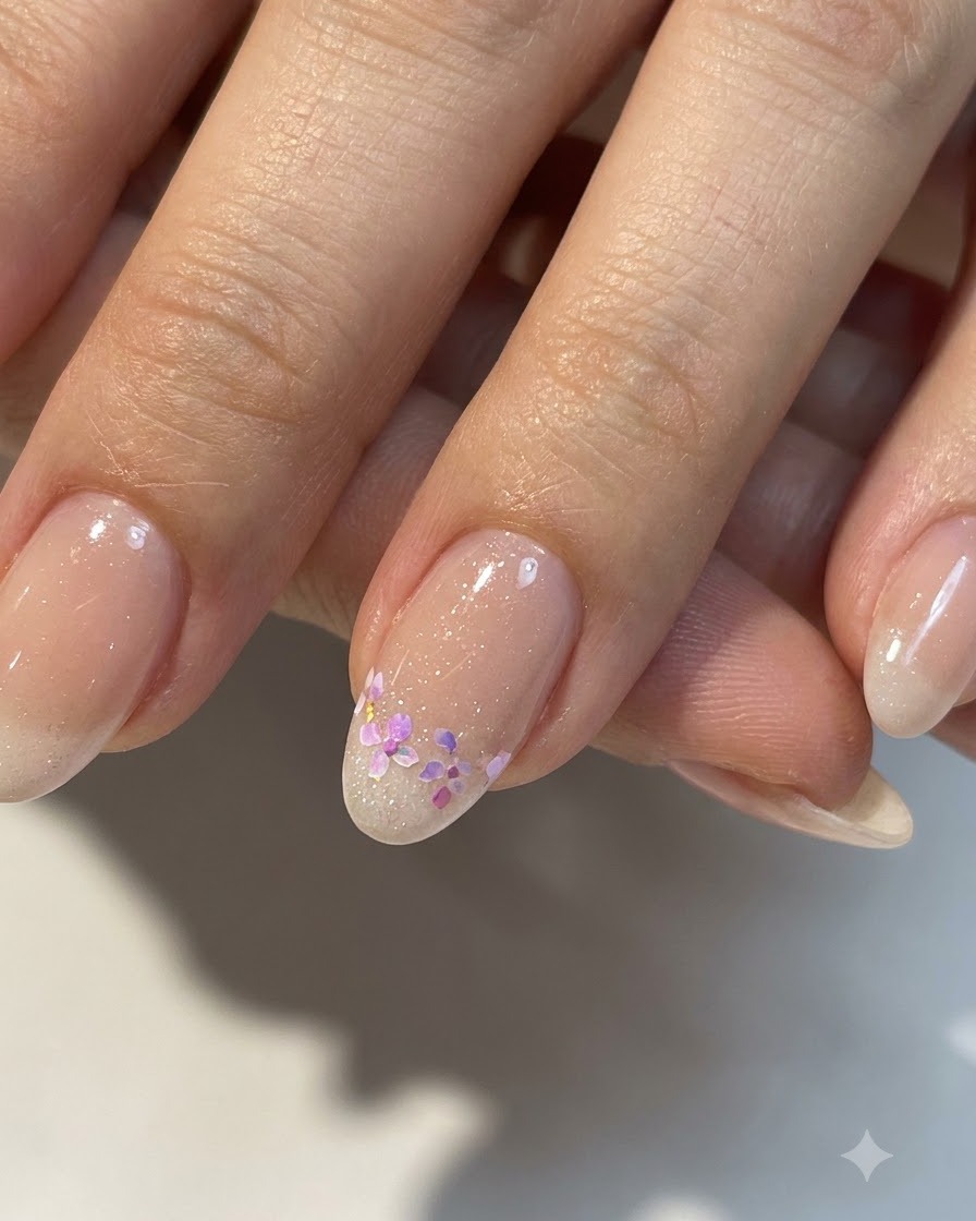 Eine Nahaufnahme von vollendeter kleiner floraler Nagelkunst auf einer glänzenden Nude-Basis mit verfeinerten Details.