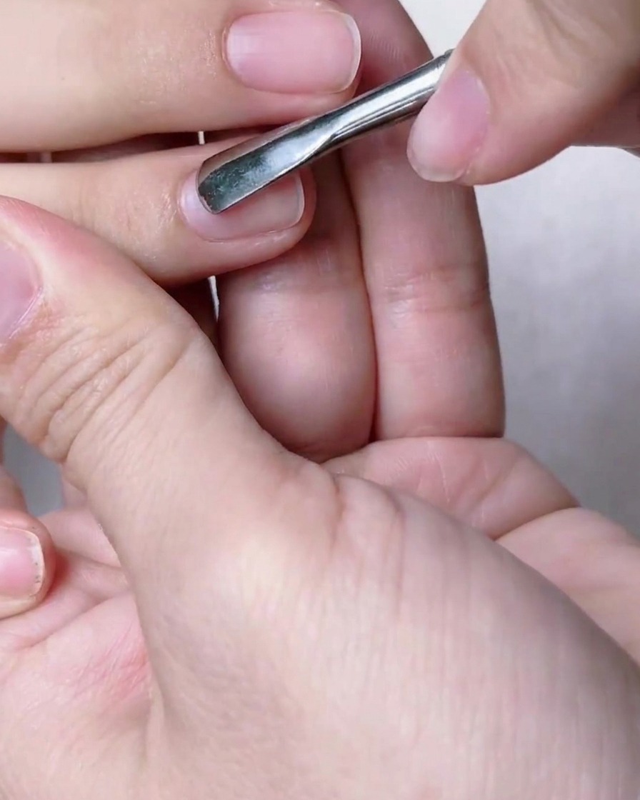 Nahaufnahme von Händen, die mit einem Metall-ProPusher die Nagelhaut sanft zurückschieben.
