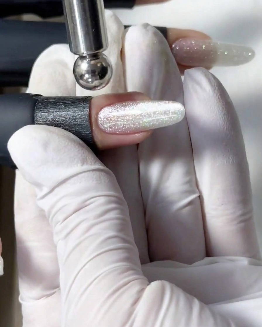 Ein zylindrischer Magnetstab schwebt über einem Glitzernagel, um die magnetischen Partikel zu einer hellen Schimmer-Linie zusammenzuziehen.