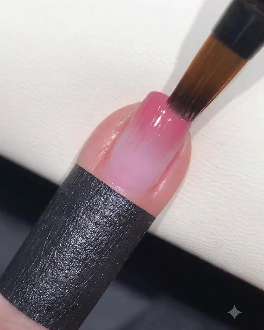 Ein Schwämmchen, das sanft rosa Gel auf einen Nagel tupft, um die Farbe in einen Verlauf zu verblenden.