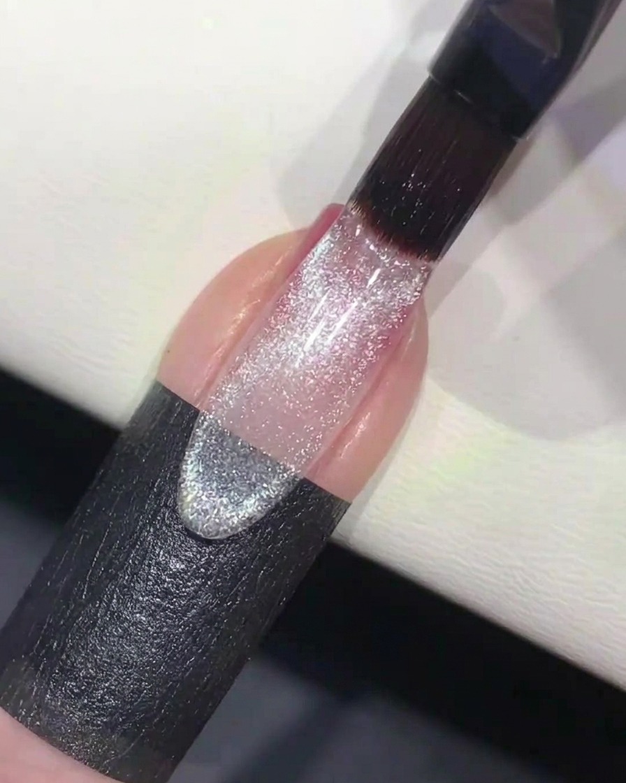Ein Nagelpinsel, der klares, glitzerndes Cat-Eye-Gel über den vorbereiteten Ombré-Nagel aufträgt.