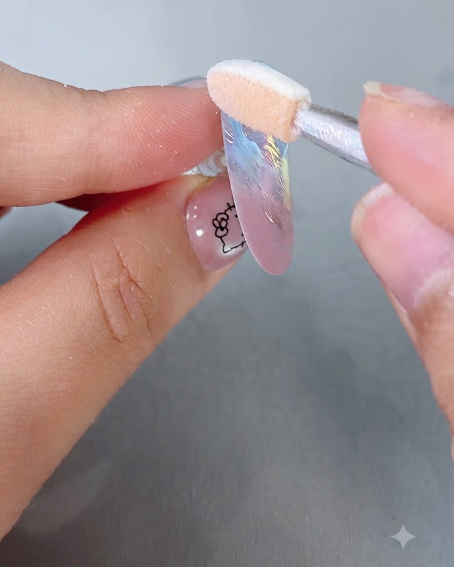Ein Schwämmchen-Applikator reibt irisierendes Magic Mirror Puder auf einen pastellfarbenen Nageltipp.