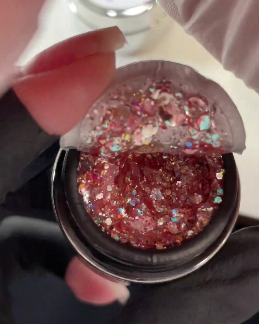 Offener Tiegel mit dickem Gel, gefüllt mit groben rosa, holografischen und Duochrom-Glitzerpailletten.