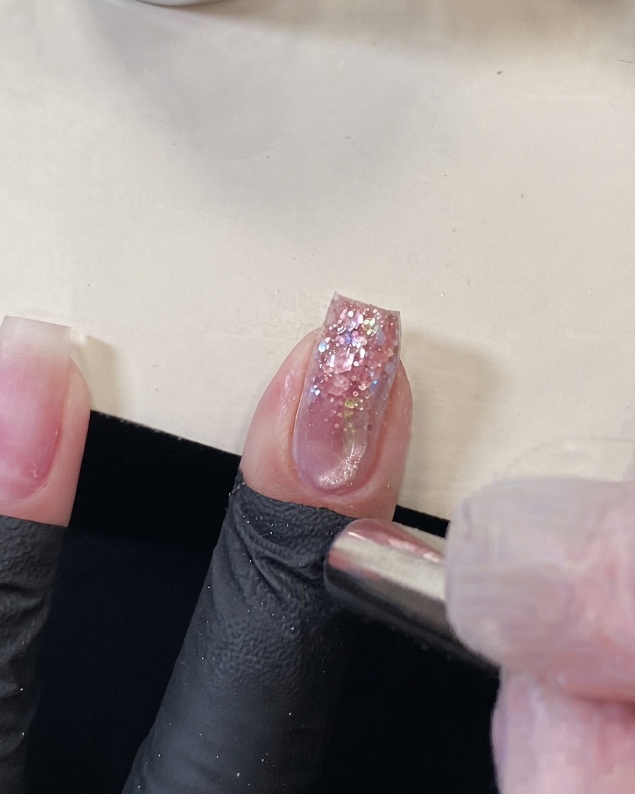 Ein zylindrischer Magnet, der in der Nähe der Spitze eines rosa Glitzernagels gehalten wird, um den magnetischen Cat-Eye-Effekt zu verschieben.