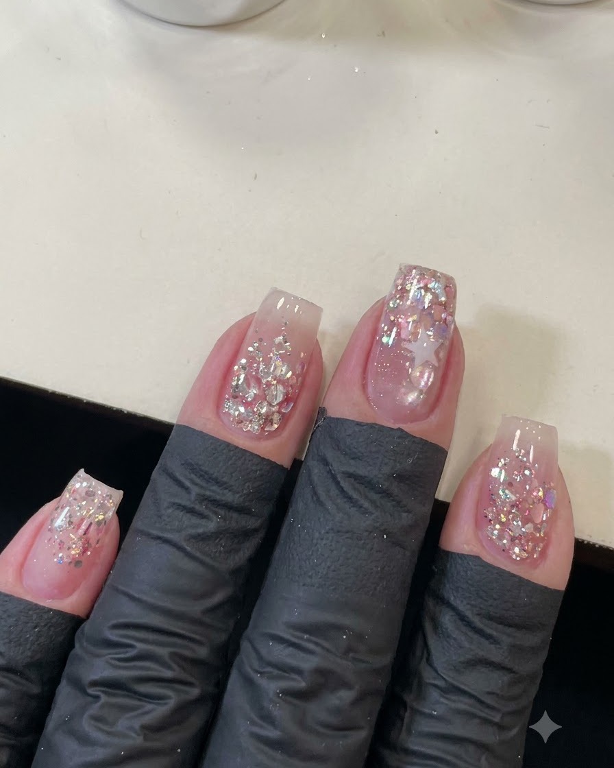 Eine Aufnahme von oben von vier manikürten Nägeln, die mit glitzernden rosa Pailletten und einer Sternumrandung dekoriert sind.