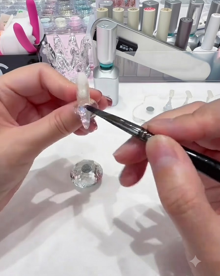 Ein kleiner Nagelpinsel lässt bunte kreisfömige Pailletten auf das feuchte Base Gel nahe der Nagelhaut fallen.