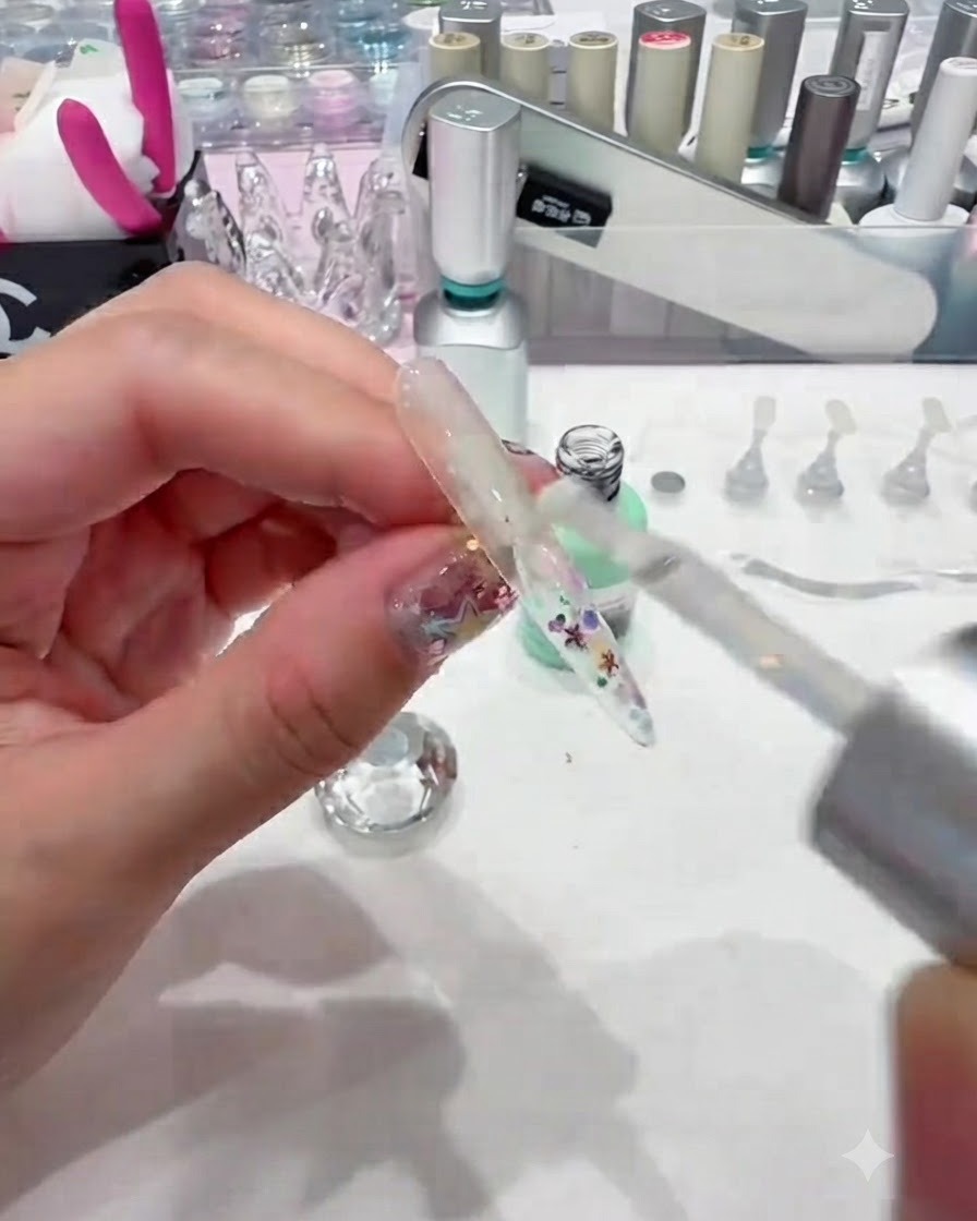 Ein Pinsel trägt eine dicke Schicht klares Builder Gel über eine paillettenbesetzte Nagelspitze auf, um sie glatt einzukapseln.