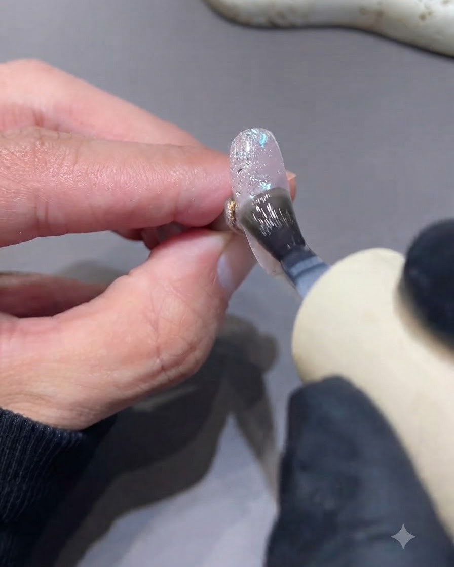 Ein Pinsel trägt einen matten Topcoat auf einen strukturierten Glitzer- und Paillettennagel auf.