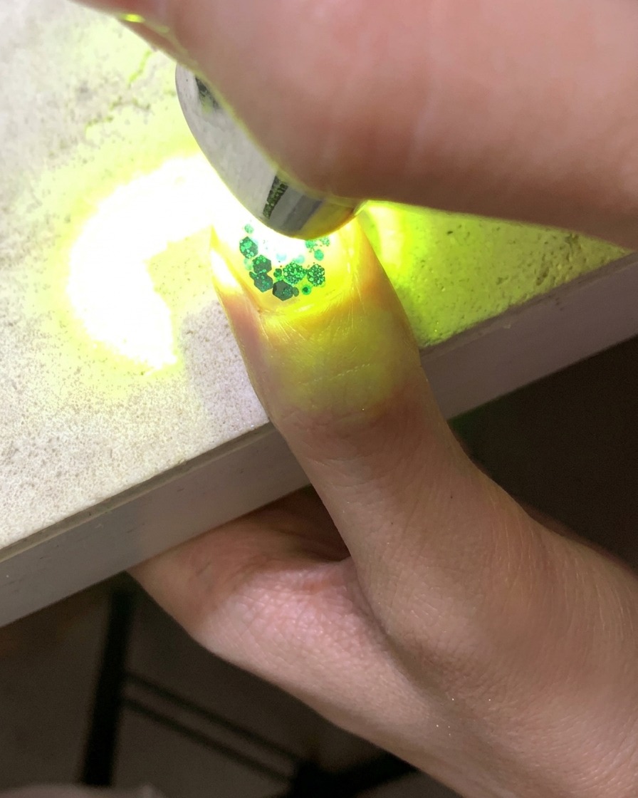 Eine Mini-UV-Lampe härtet einen Nagel aus, der mit Glitter und hohlen Sternenpailletten verziert ist.