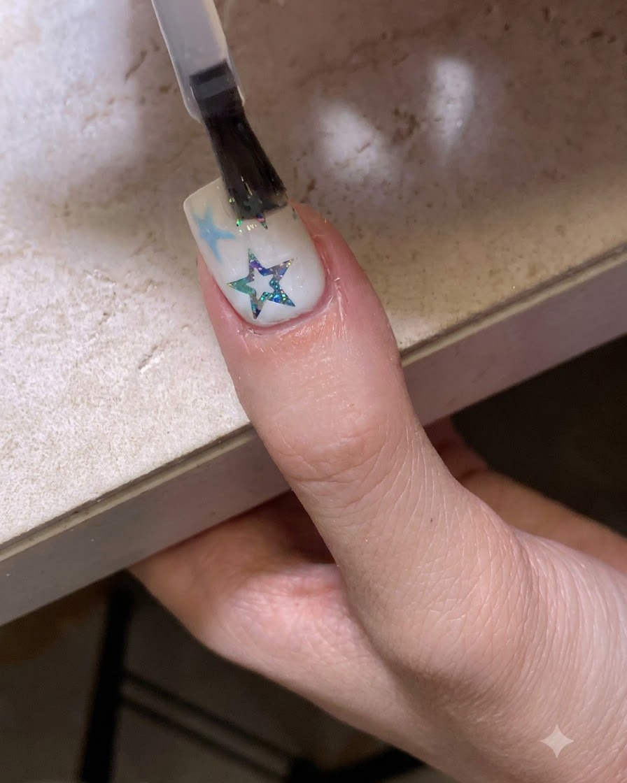 Ein Pinsel trägt einen glänzenden, klaren Top Coat über einen mit Sternen und Glitter verzierten Nagel auf.