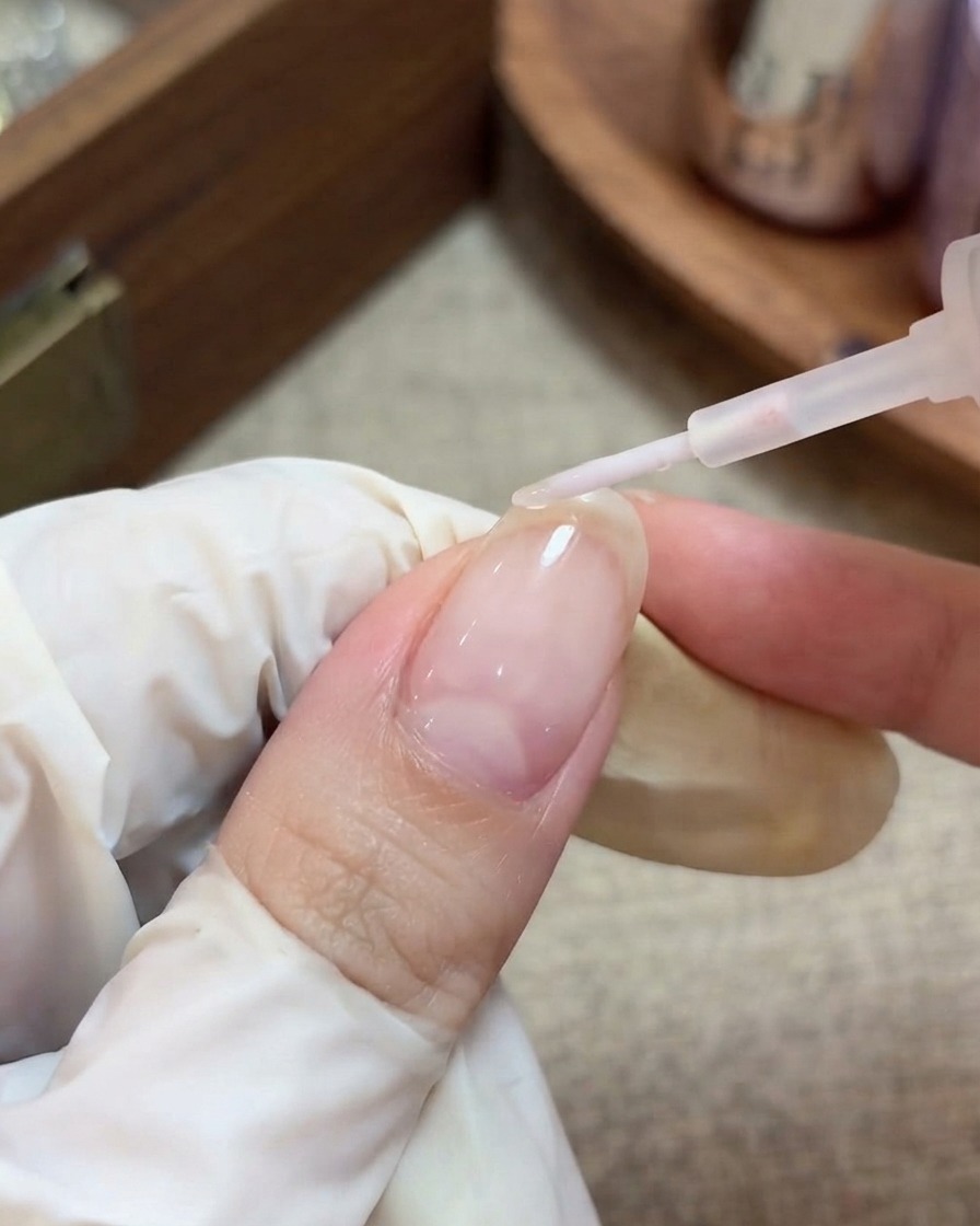 Eine behandschuhte Hand verwendet einen Pinsel, um einen klaren, glänzenden Top Coat auf einen vorbereiteten Nagel mit eingekapselten Stern-Glitzern aufzutragen.
