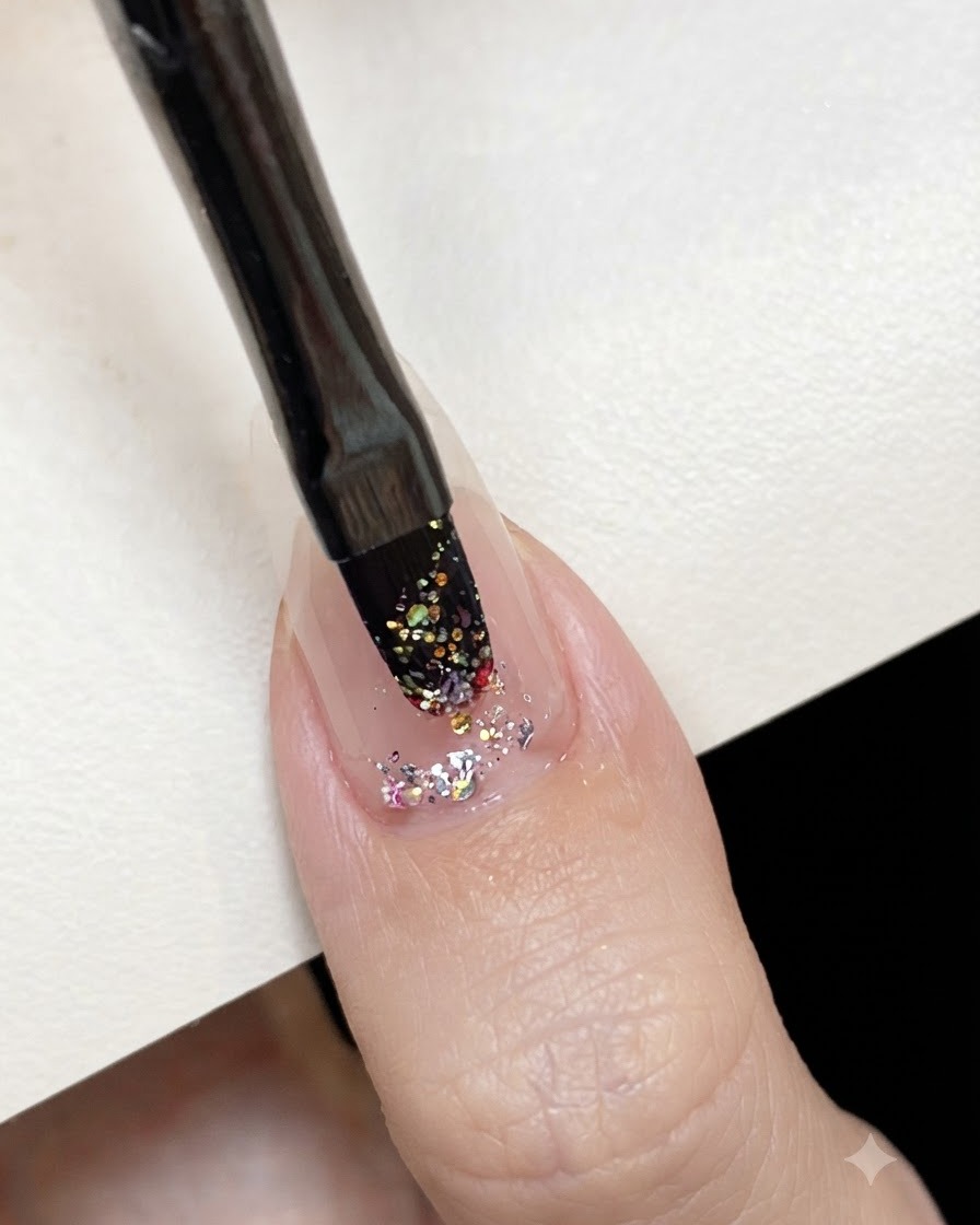 Ein flacher Gelpinsel tupft pinkes holografisches Glitter-Gel auf die Mitte eines vorbereiteten Nagels.