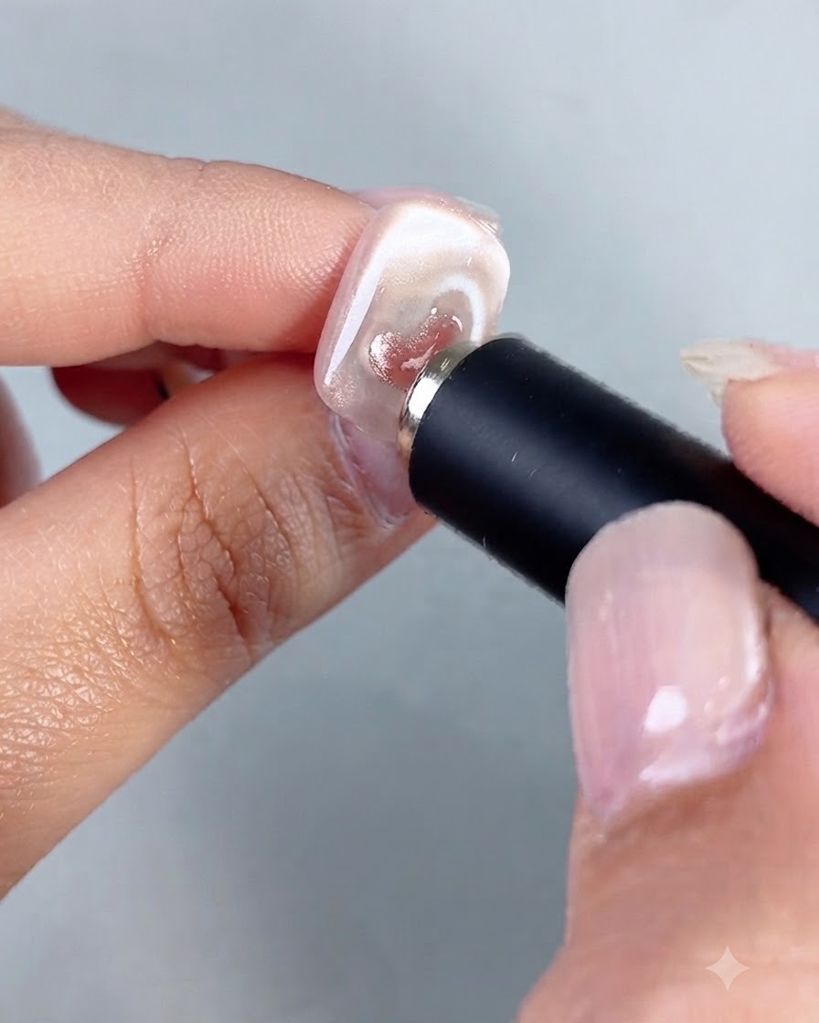 Ein zylindrisches Magnetwerkzeug wird nahe an einen Nagel gehalten, um den Schimmer in einem kleinen aufgemalten Cat-Eye-Herz zu konzentrieren.