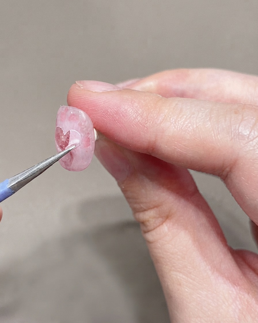 Ein feiner Pinsel trägt eine zweite Schicht sehr hellen Rosagels auf den vorbereiteten Nagel auf.