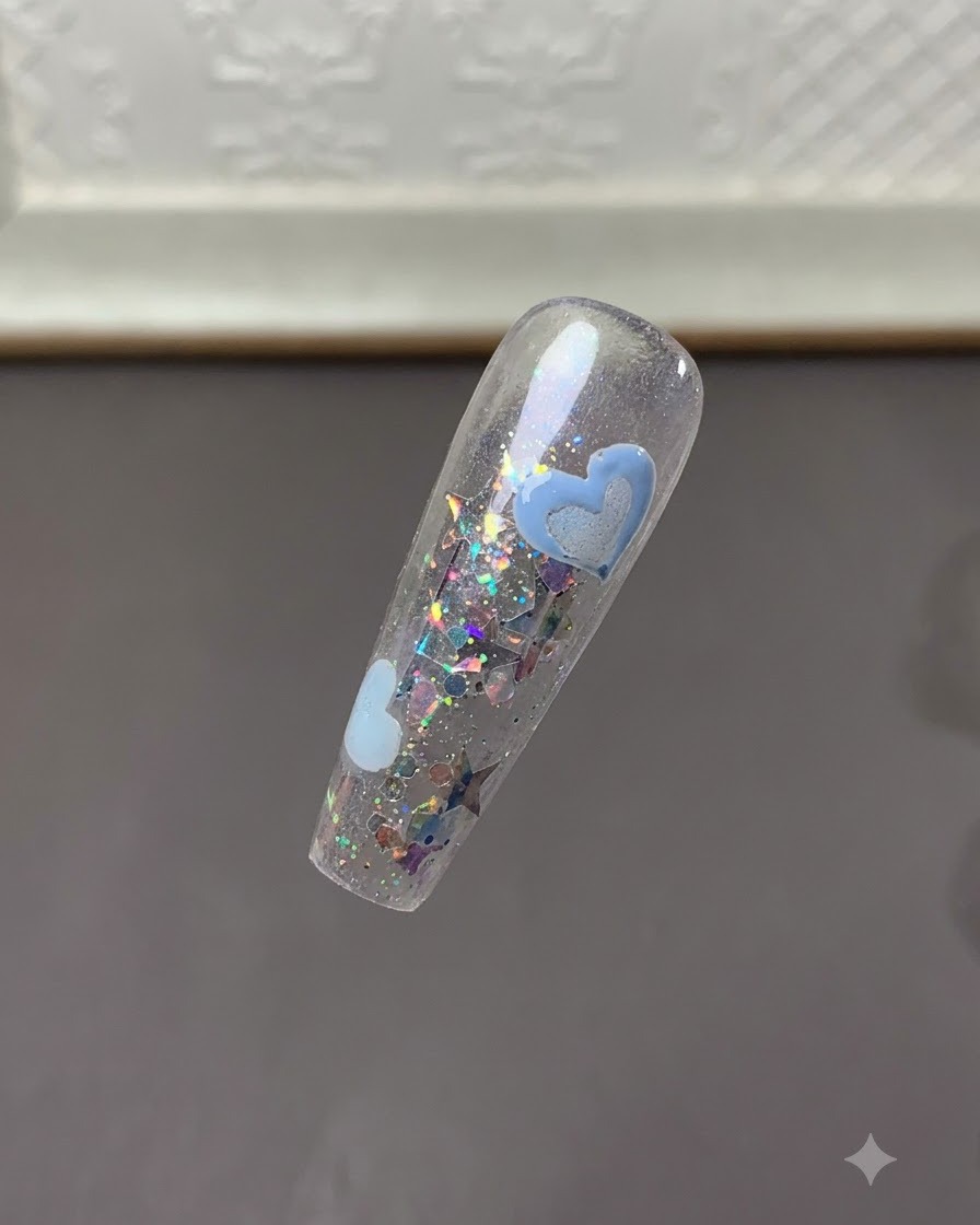 Eine klare Ansicht der Nagelspitze, die ausgehärtete hellblaue Herzdesigns inmitten von Glitzerflocken zeigt.