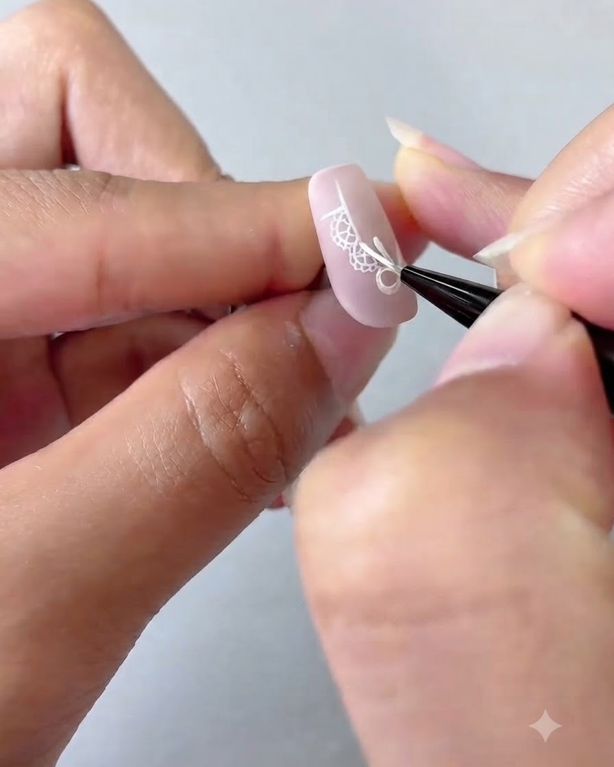 Ein Nail-Art-Pinsel fügt detaillierte weiße Punkte und einen vierzackigen Stern auf einem rosa Ombré-Nagel hinzu.