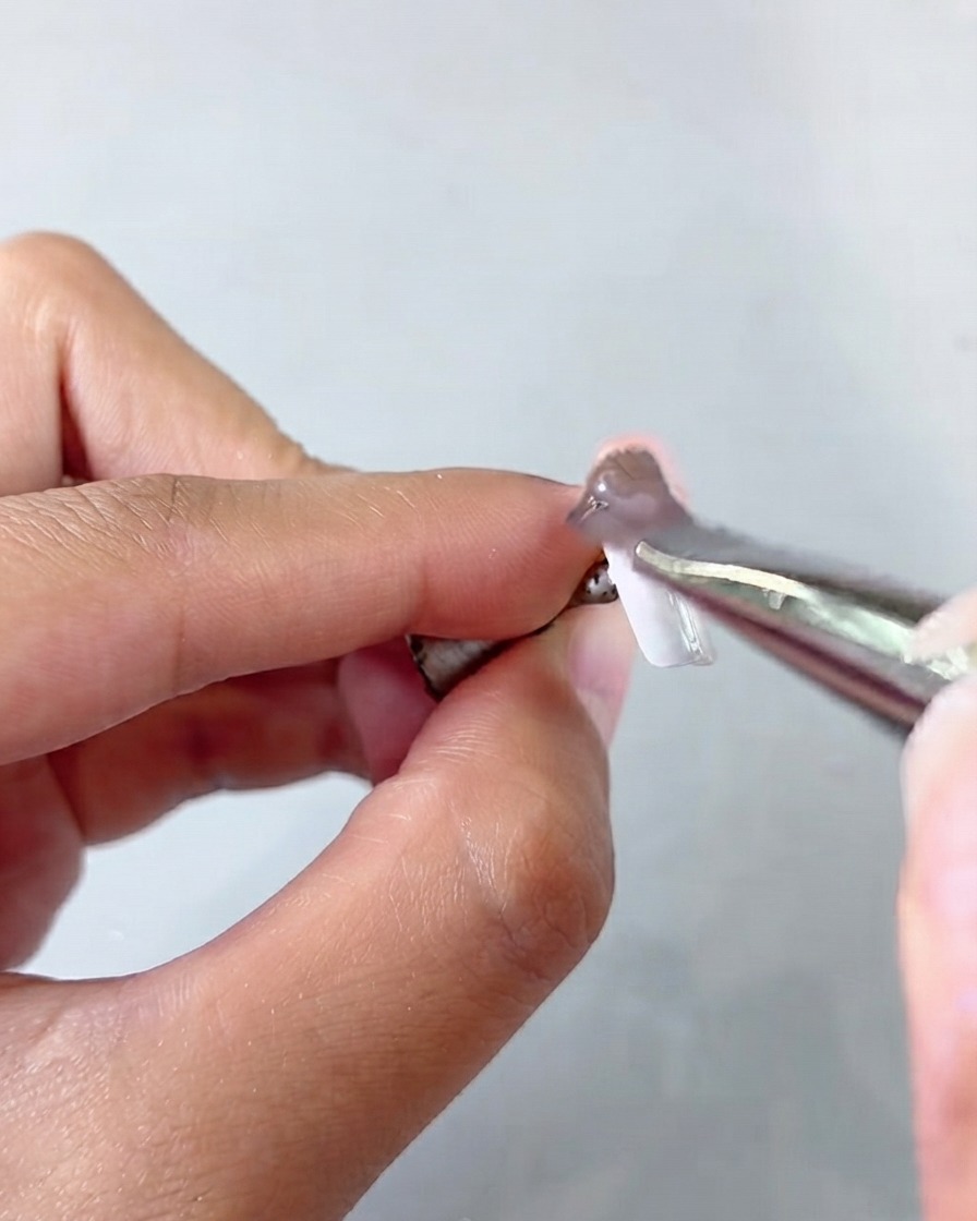 Eine Pinzette hält einen Nageltipp, während eine Schicht Cat Eye Gel aufgetragen wird.