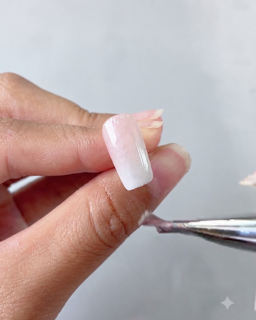 Eine Hand hält einen Pinsel und trägt einen milchig weißen Cat Eye Gel Basis-Coat auf einen Nagel auf.