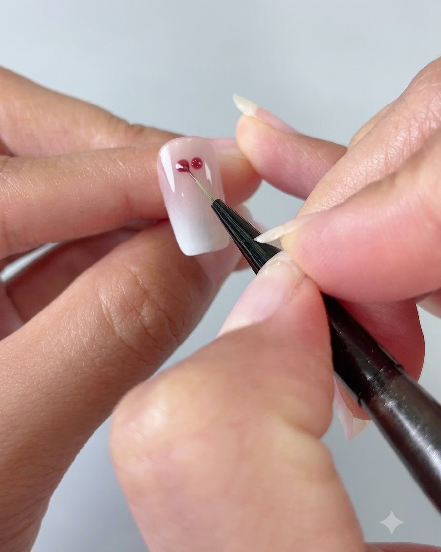 Ein feiner Nail-Art-Pinsel verbindet zwei rote Gel-Punkte zu einer Herzform auf einem Cat-Eye-Nagel mit Verlauf.