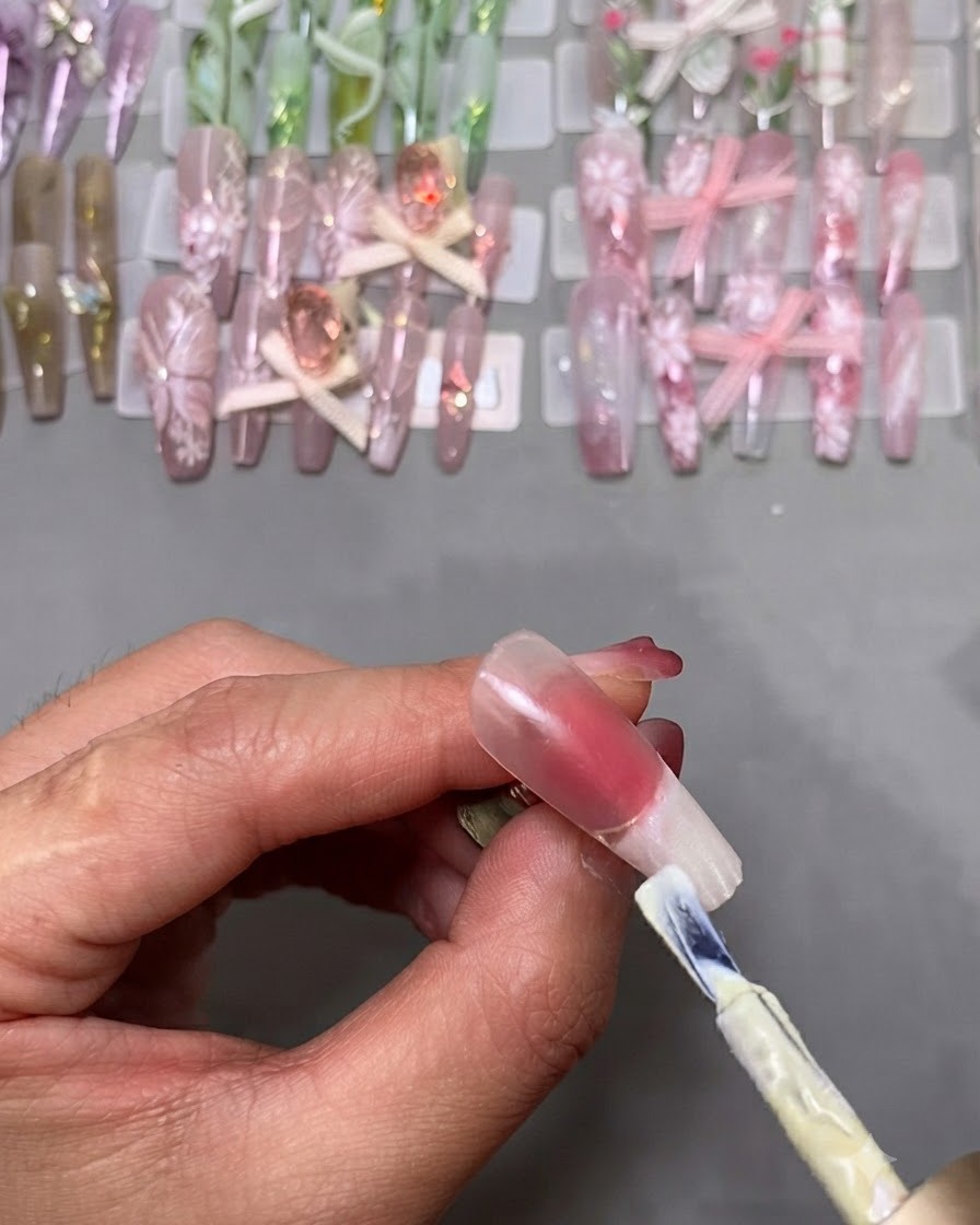 Ein Gel-Nagellackpinsel trägt weißen Lack auf die Spitze eines auf einem Ständer montierten Kunstnagels auf.