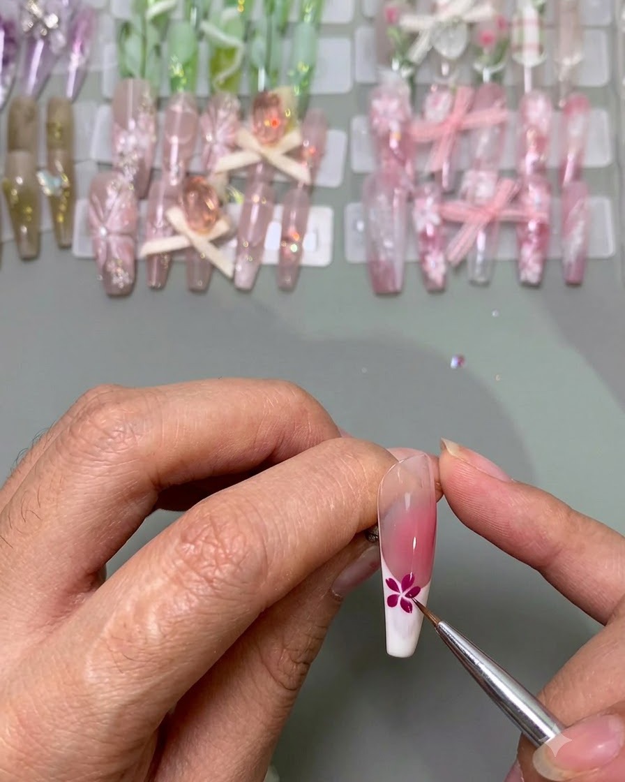 Ein feiner Pinsel fügt blaue Blütenblätter neben einer vollendeten pinken Blume auf einer Nagelspitze hinzu.