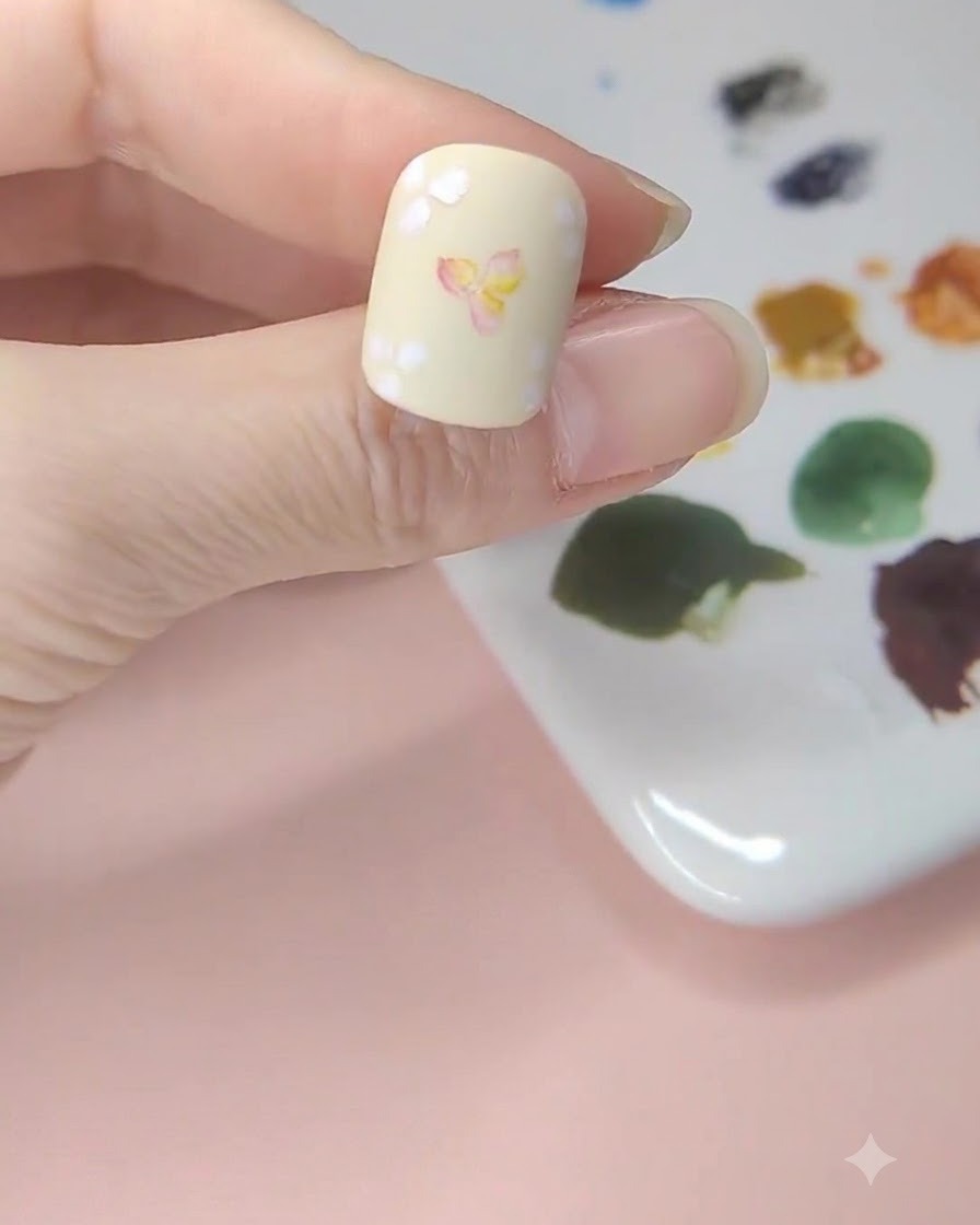 Ein blassgelber Nagel, auf dem gelbe Aquarell-Lasuren in den leeren Räumen um die florale Kunst herum aufgetragen werden.