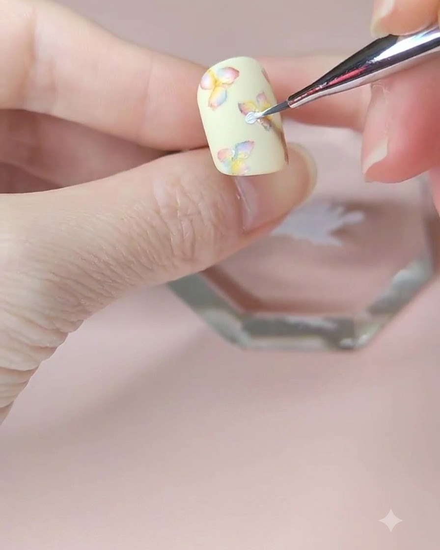 Nahaufnahme eines feinen Nailart-Pinsels, der eine zweite Schicht weißer Blütenblätter auf die mittlere Blume aufträgt.