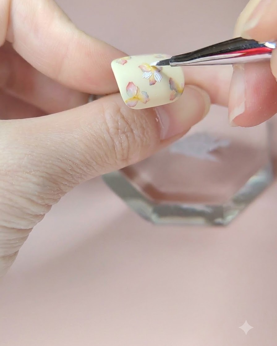 Ein feiner Pinsel trägt eine zweite Schicht weißer Blütenblätter auf die obere linke Blume des Nagels auf.