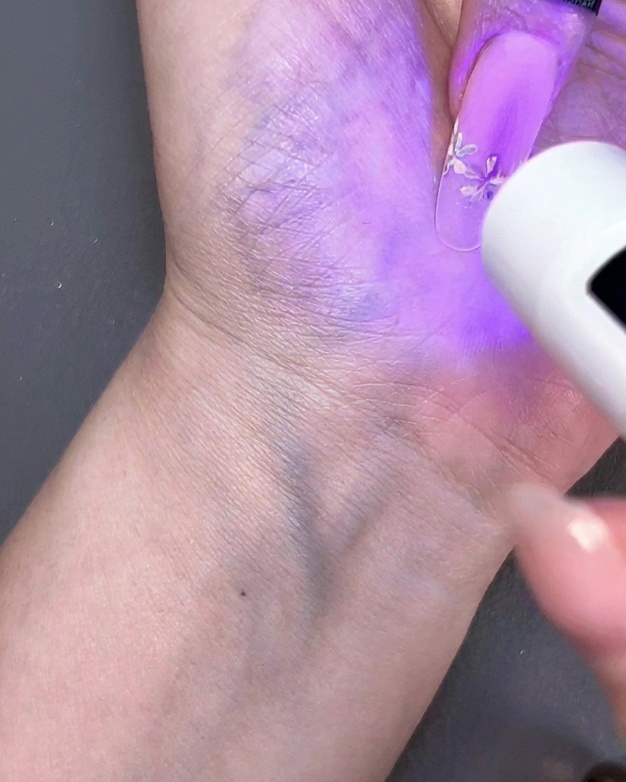 Eine tragbare Mini-UV-Lampe, die ein florales Nageldesign unter violettem Licht aushärtet.