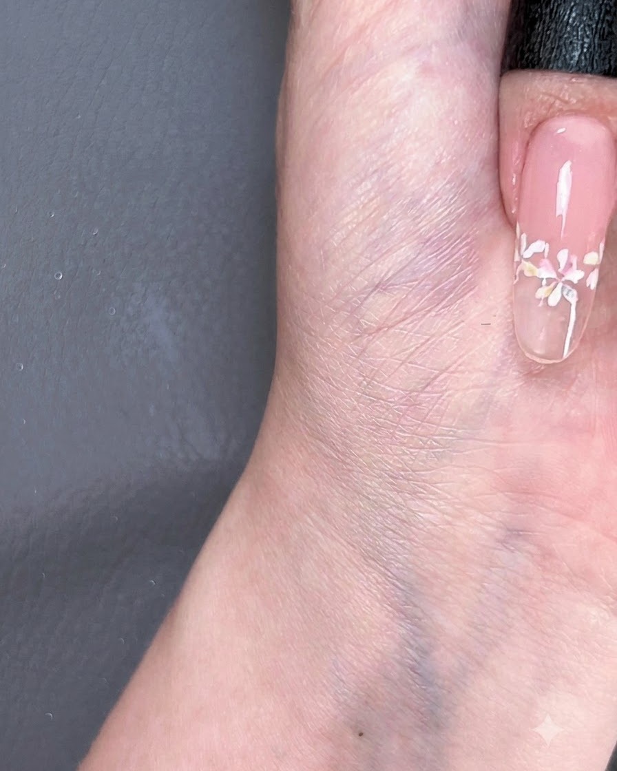 Ein Pinsel gleitet mit einem glänzenden Überlack über ein fertiges French-Blumen-Nageldesign.