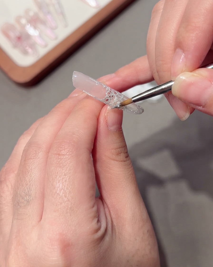 Ein feiner Liner-Pinsel zieht silberne Glitzer-Spinn-Gel-Fäden entlang des Nagelrands.