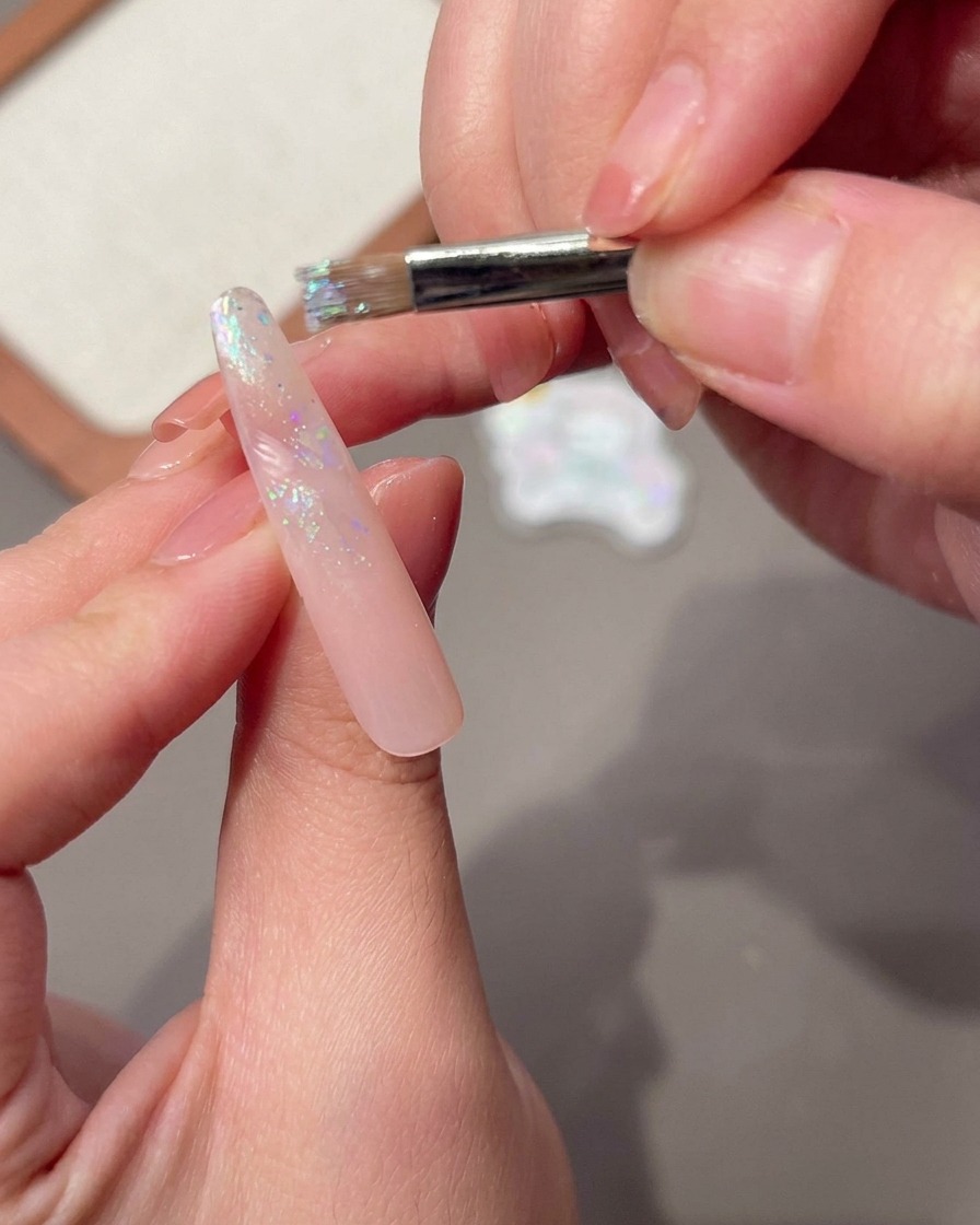 Ein Nagelpinsel trägt eine nasse Schicht Base-Gel auf einen langen rosa Nagel auf.