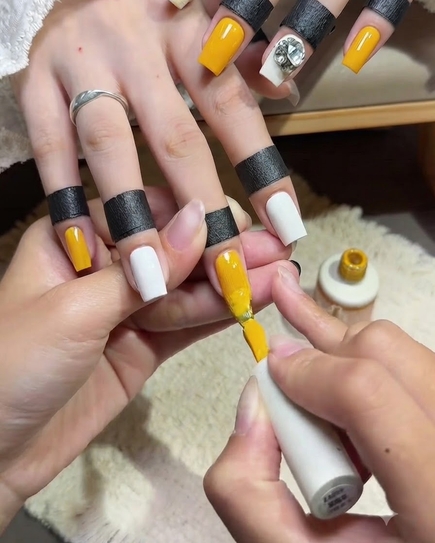 Eine Nahaufnahme einer Nageldesignerin, die eine glatte zweite Schicht hellgelben Gel-Lacks mit dem Pinsel auf einen Zeigefinger aufträgt.