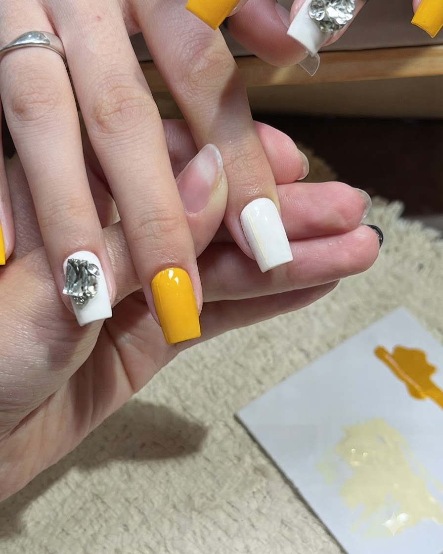 Ein Nagelkunstpinsel trägt eine zweite dünne horizontale gelbe Linie auf einen weißen Nagel auf.
