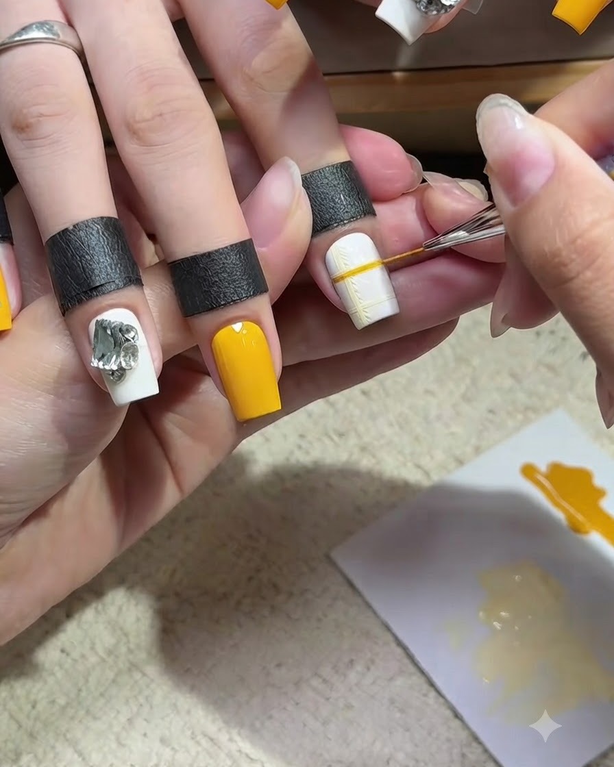 Ein feiner Liner-Pinsel zieht eine gelbe, sich kreuzende Linie über eine weiße Nagelbasis und vervollständigt ein zartes gelbes Karogittermuster.