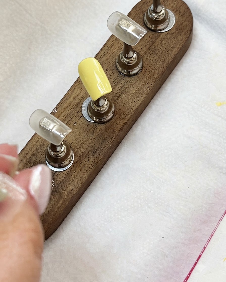 Nagelspitzen auf einem Holzständer zeigen eine milchig gelbe Spitze und Nude-farbene Spitzen.