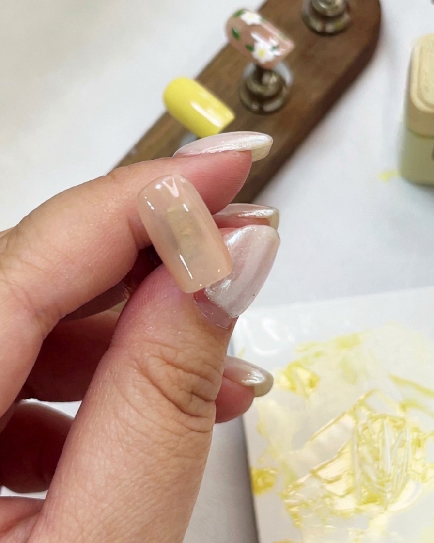 Eine Nahaufnahme einer Hand, die eine Nude-farbene Nagelspitze hält und Cat-Eye-Gel aufträgt.