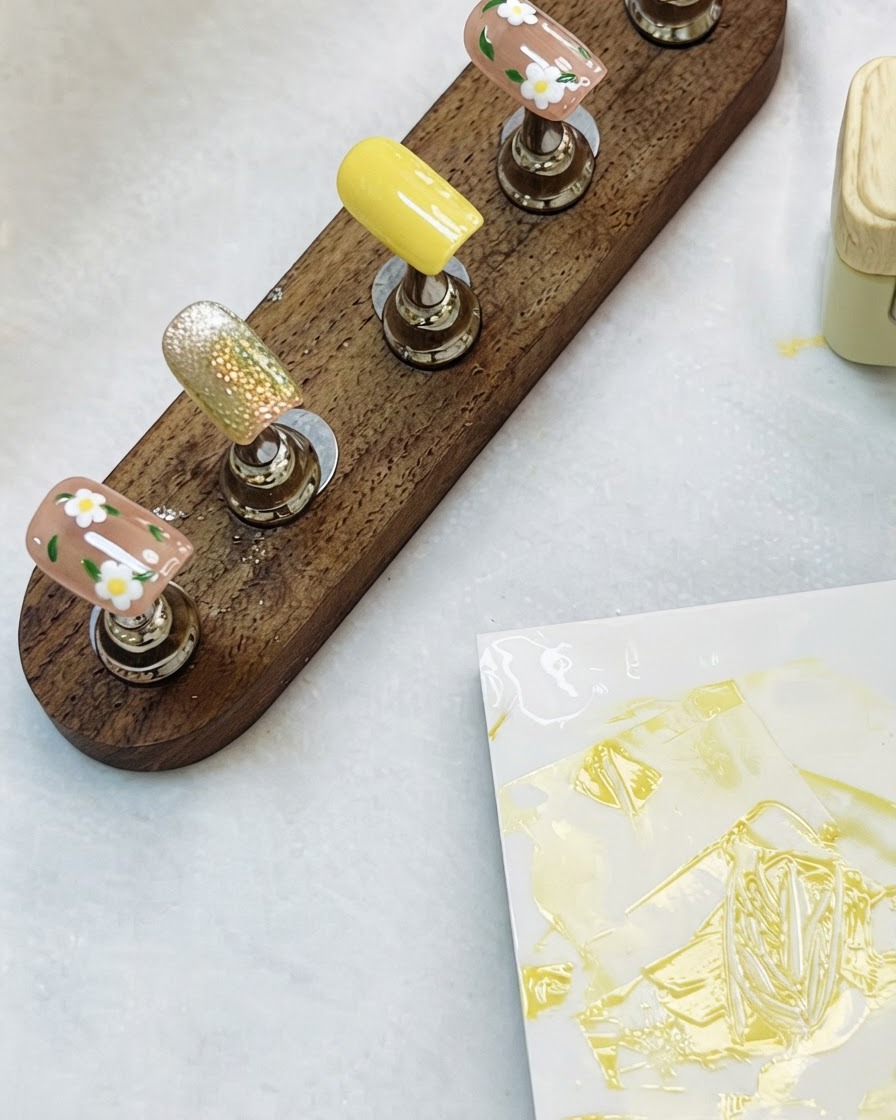 Ein Holzdisplayständer mit fertigen floralen und Cat-Eye-Nagelkunstspitzen auf einem Tisch.