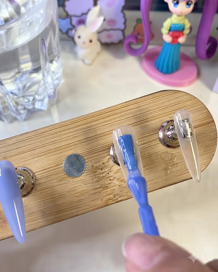 Ein Pinsel trägt kräftig blaues Gel-Polish auf einen künstlichen Nageltip auf einem Holzständer auf, neben einem Nagel mit milchig weißer Basis.
