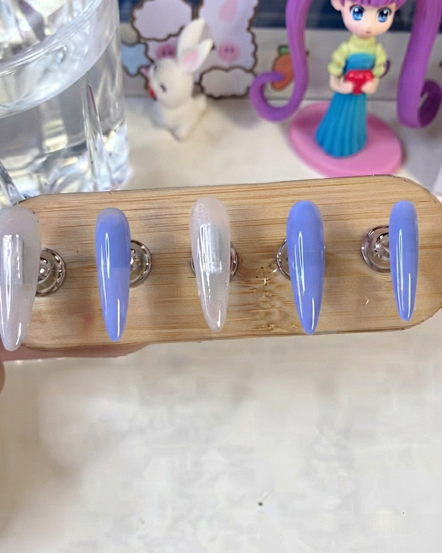 Ein Nagelständer zeigt blau und milchig weiß lackierte Nägel, die unter einer UV- und LED-Lampe aushärten.