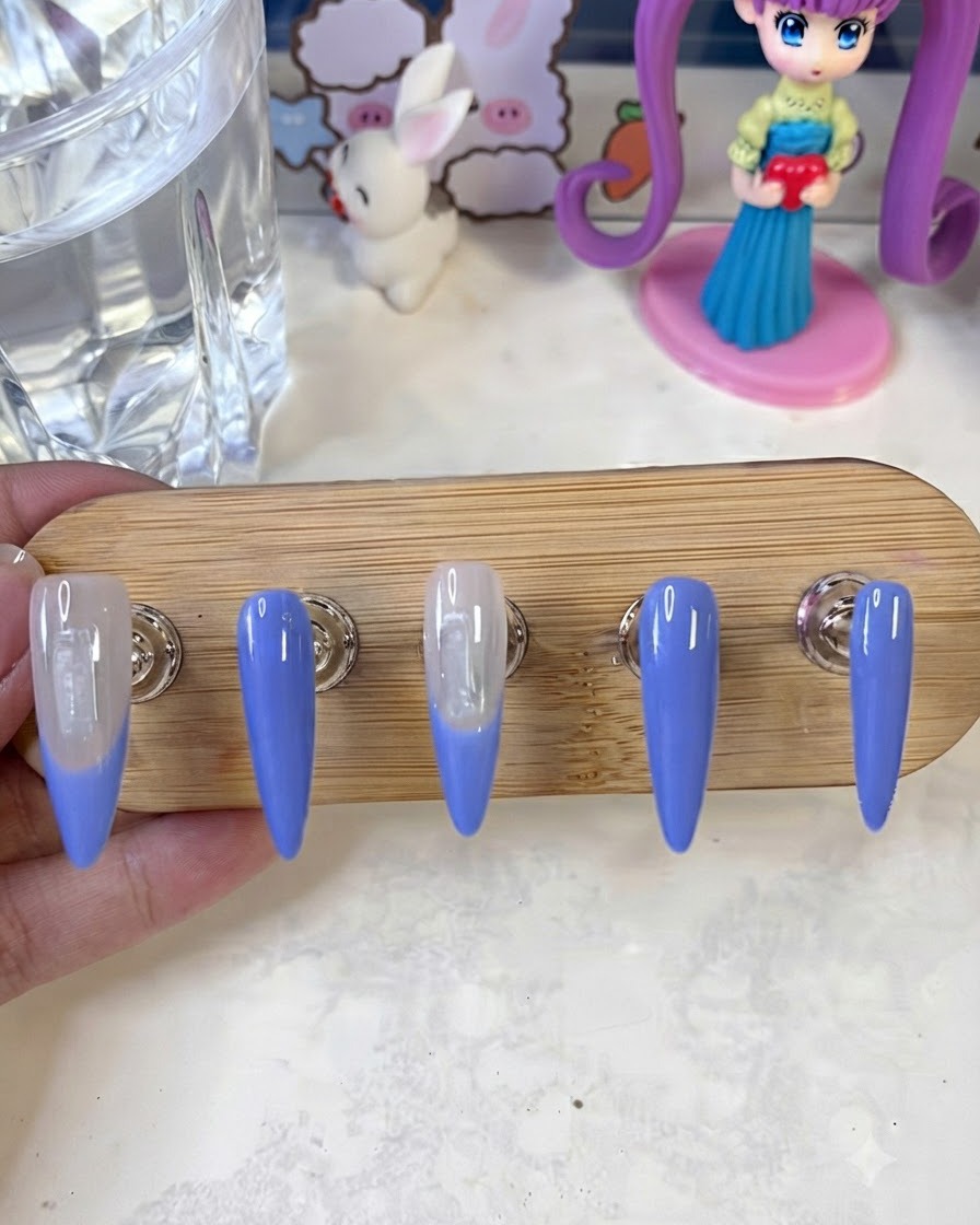 Ein Nail-Art-Pinsel trägt eine zweite Schicht der blauen French-Tip-Farbe auf die Nagelränder auf einem Display-Ständer auf.
