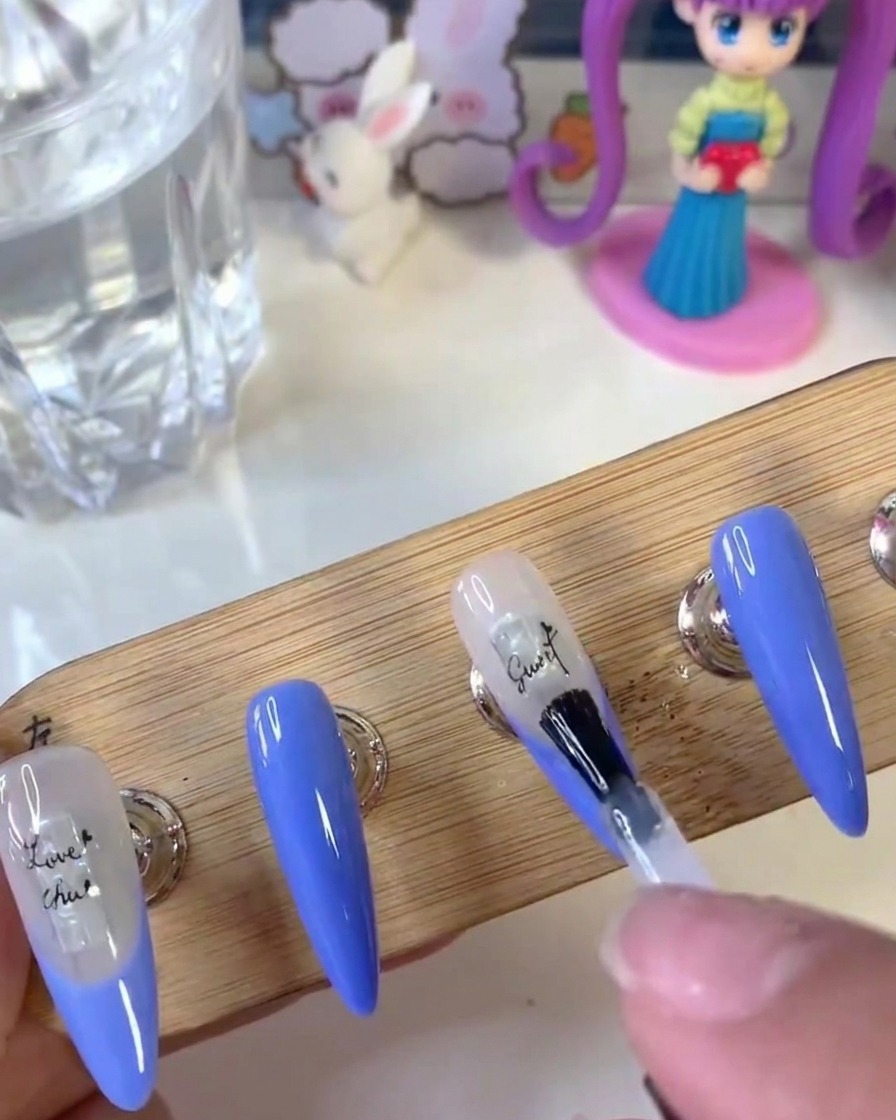 Ein Nagelpinsel trägt eine klare Schicht Verstärkungsgel gleichmäßig über eine Nageloberfläche mit Buchstaben-Stickern auf.