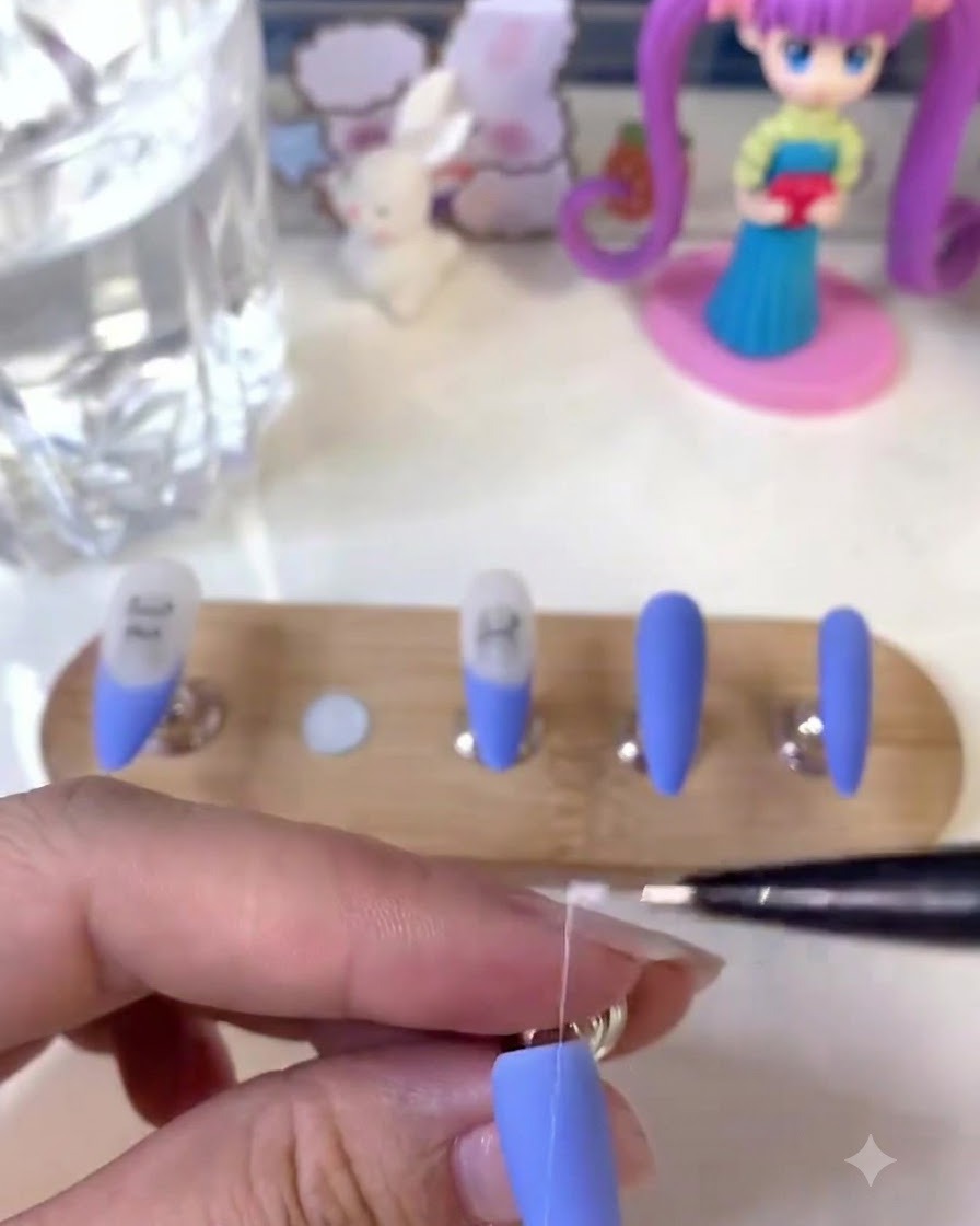 Eine Nageldesignerin hält einen feinen Liner-Pinsel und zeichnet detaillierte weiße Linien auf einen matten blauen Nagel.